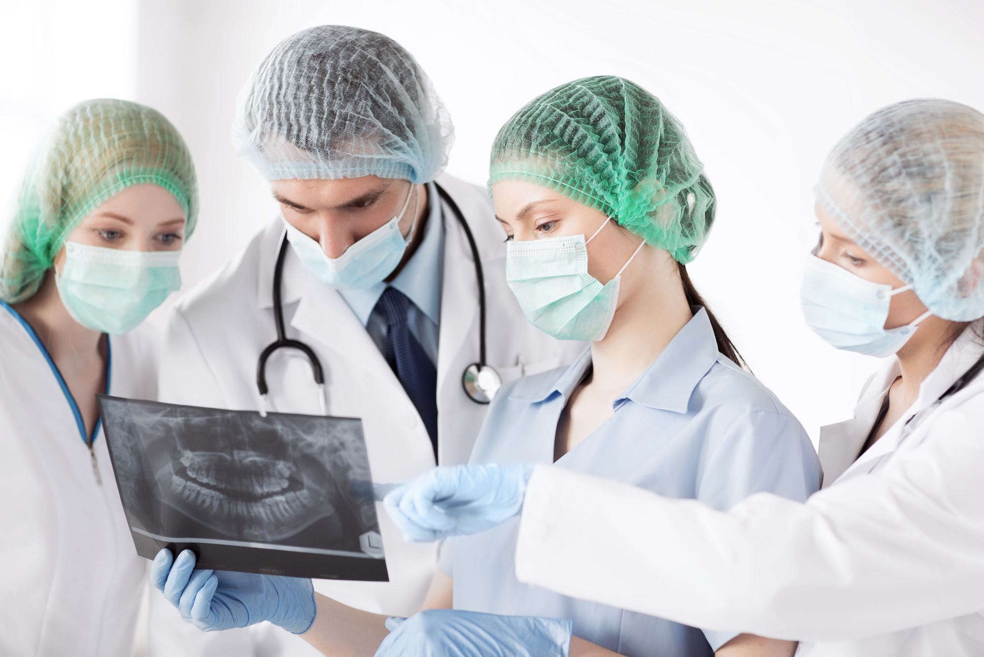 three doctors in white lab coats with gloves viewing jaw surgery xray