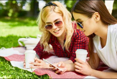 two young women looking at phone drinking coffee